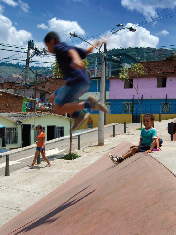 Children playing on a slope. A girl is sitting smiling while a boy is jumping off it.
