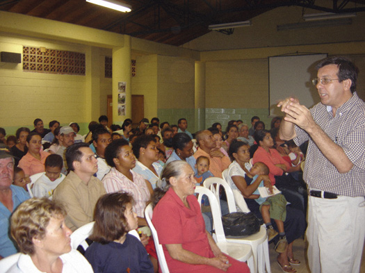 An assembly hall showing rows of people learning about the project from a speaker standing at the front of the room