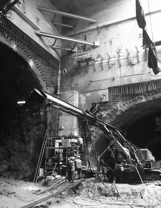 A black and white photo of men building a tunnel with hard hats, scaffolding, and construction equipment