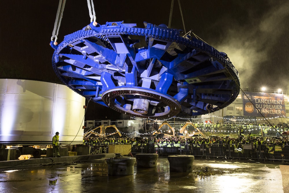 A large blue tunneller's cutting wheel is raised off the ground by cables.